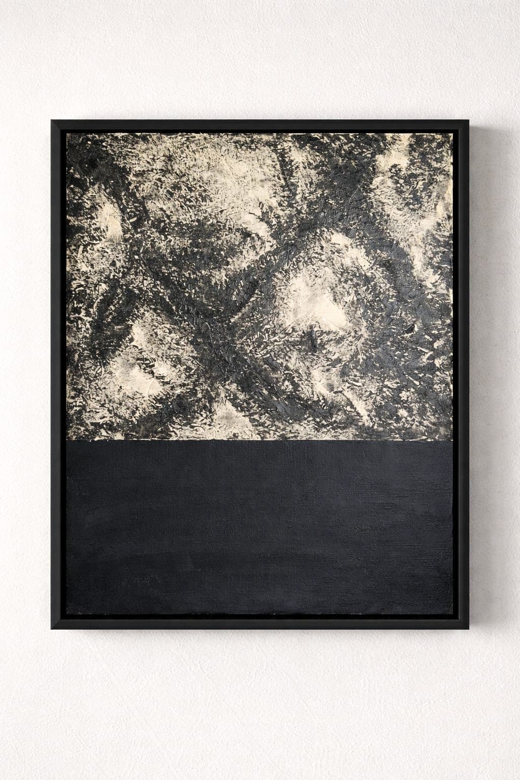 Black River — Een abstract schilderij in tweeën gedeeld — een dicht, gevlekt veld van zwart-crème textuur boven een stille band van diep houtskoolgrijs, als een kolkende kust die donker water ontmoet. In zwarte lijst.