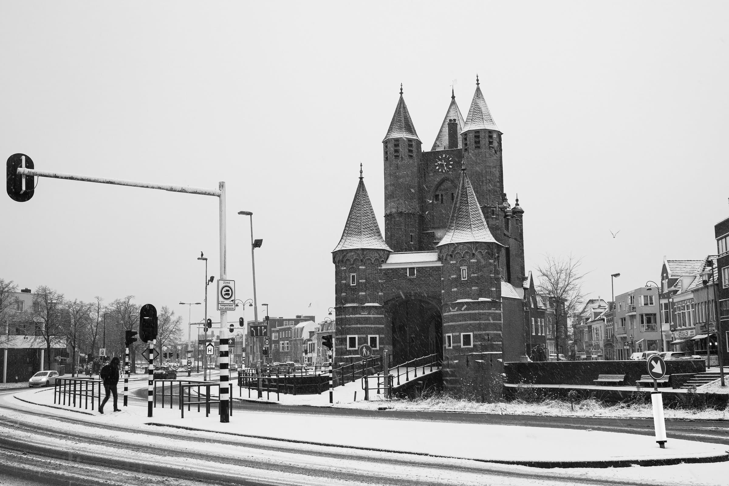 Winter Gate — De Amsterdamse Poort in Haarlem tijdens een stille sneeuwbui. De stad vertraagt; het middeleeuwse silhouet houdt stand tussen verkeerslichten en voorbijgangers.